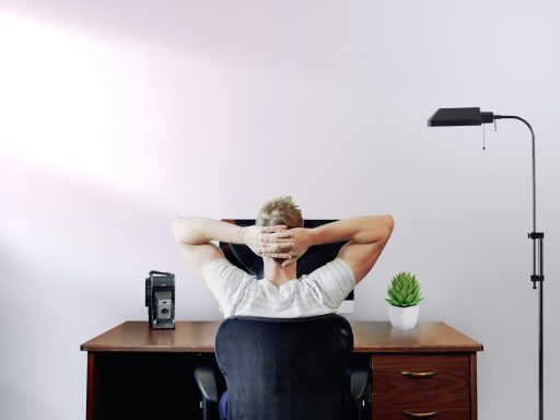 man holding his head while sitting on chair near computer desk