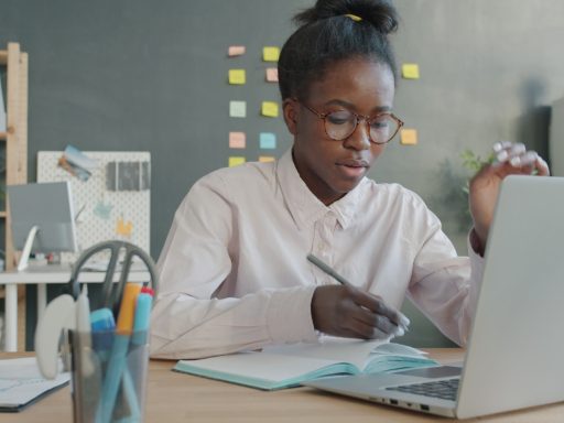 Woman working at a desk with laptop and notebook.